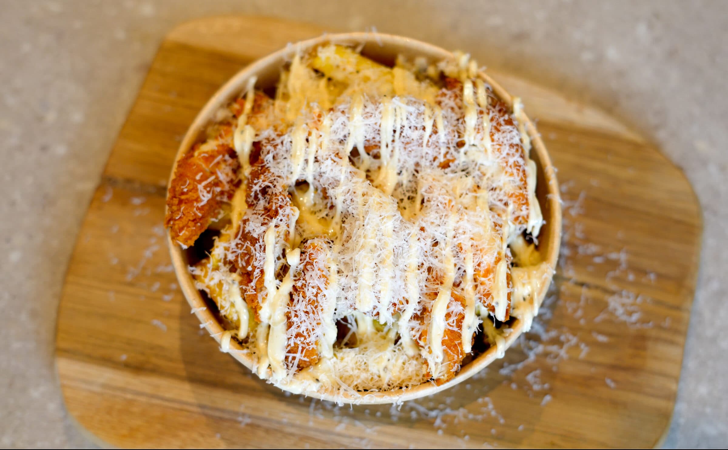 Loaded fries met truffelmayo, geraspte parmezaan en bieslook in een kraft bakje op een houten plank