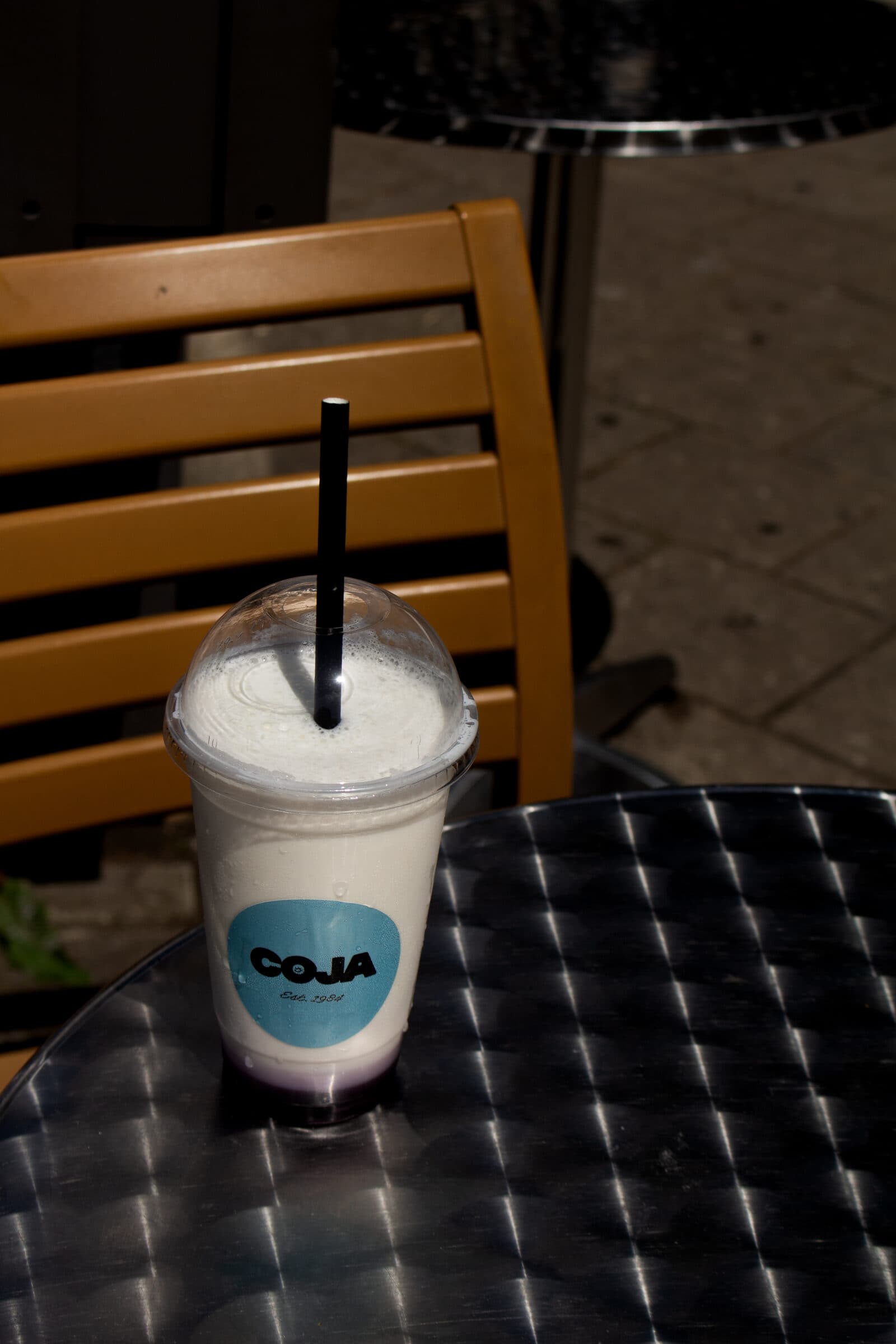Coja milkshake met foam en rietje op een metalen terrastafeltje in de zon