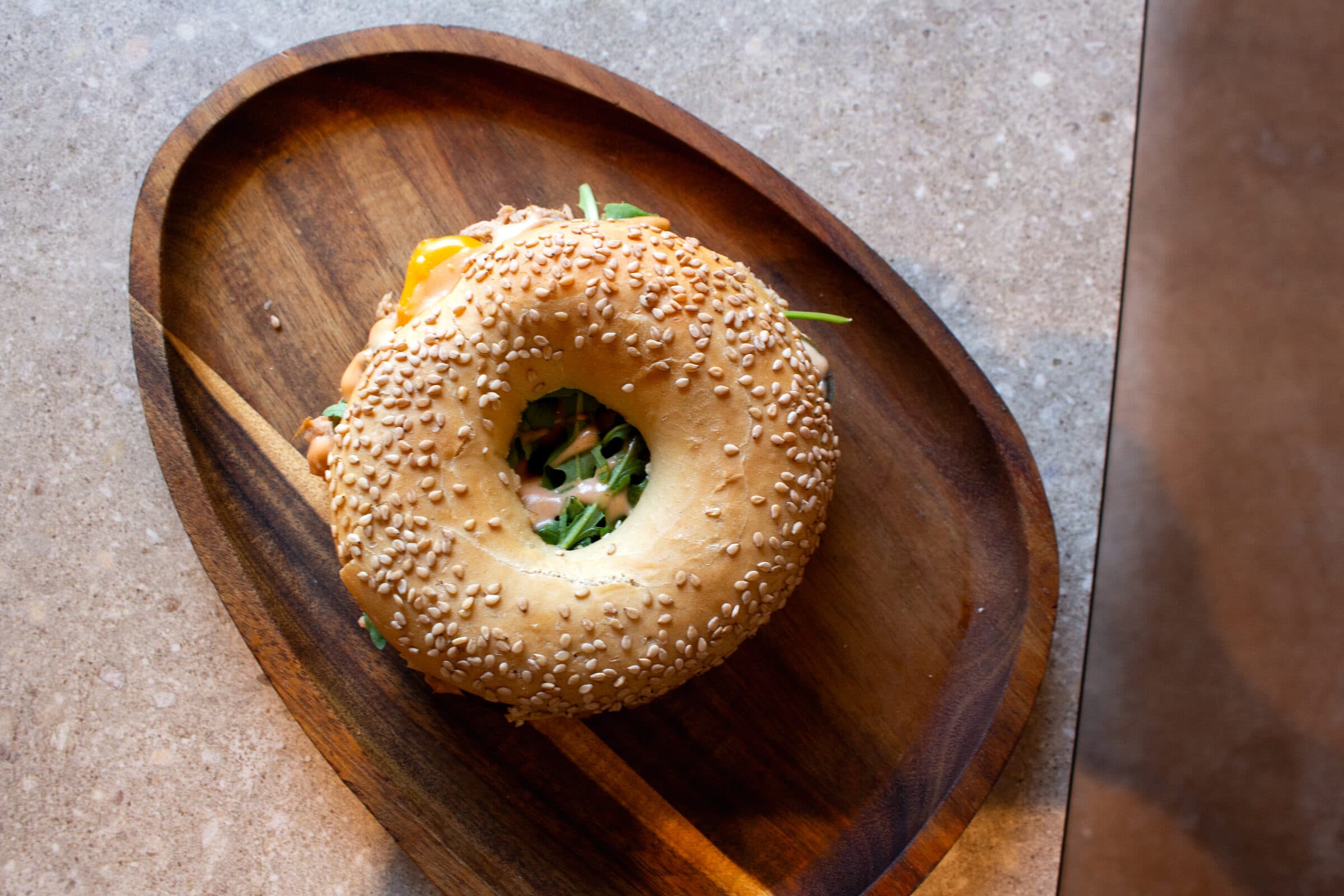 Sesambagel met tonijn en rucola op een houten schaaltje, van boven.