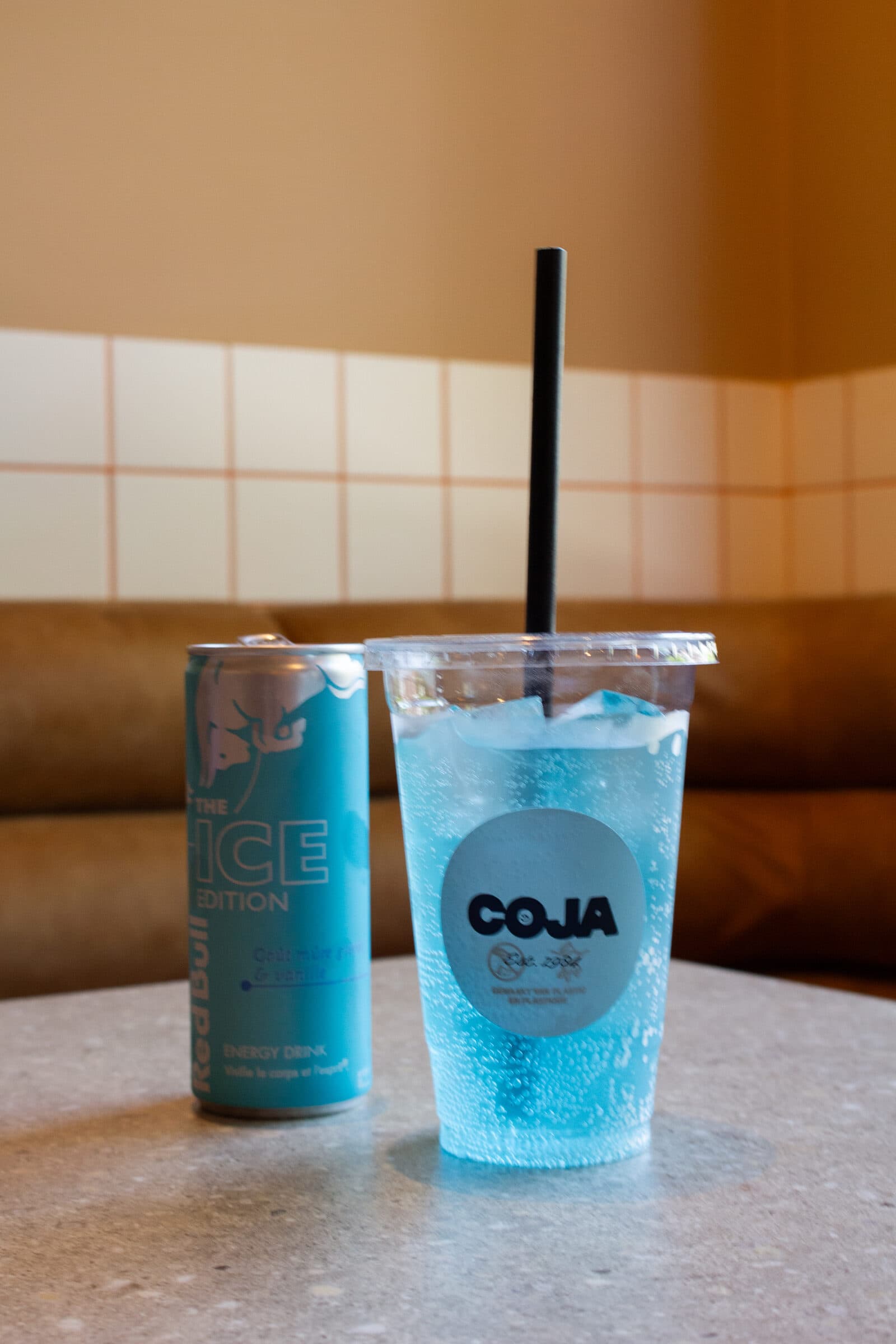Een blauwe Coja frisdrank met rietje op een terrazzo tafeltje in het interieur.