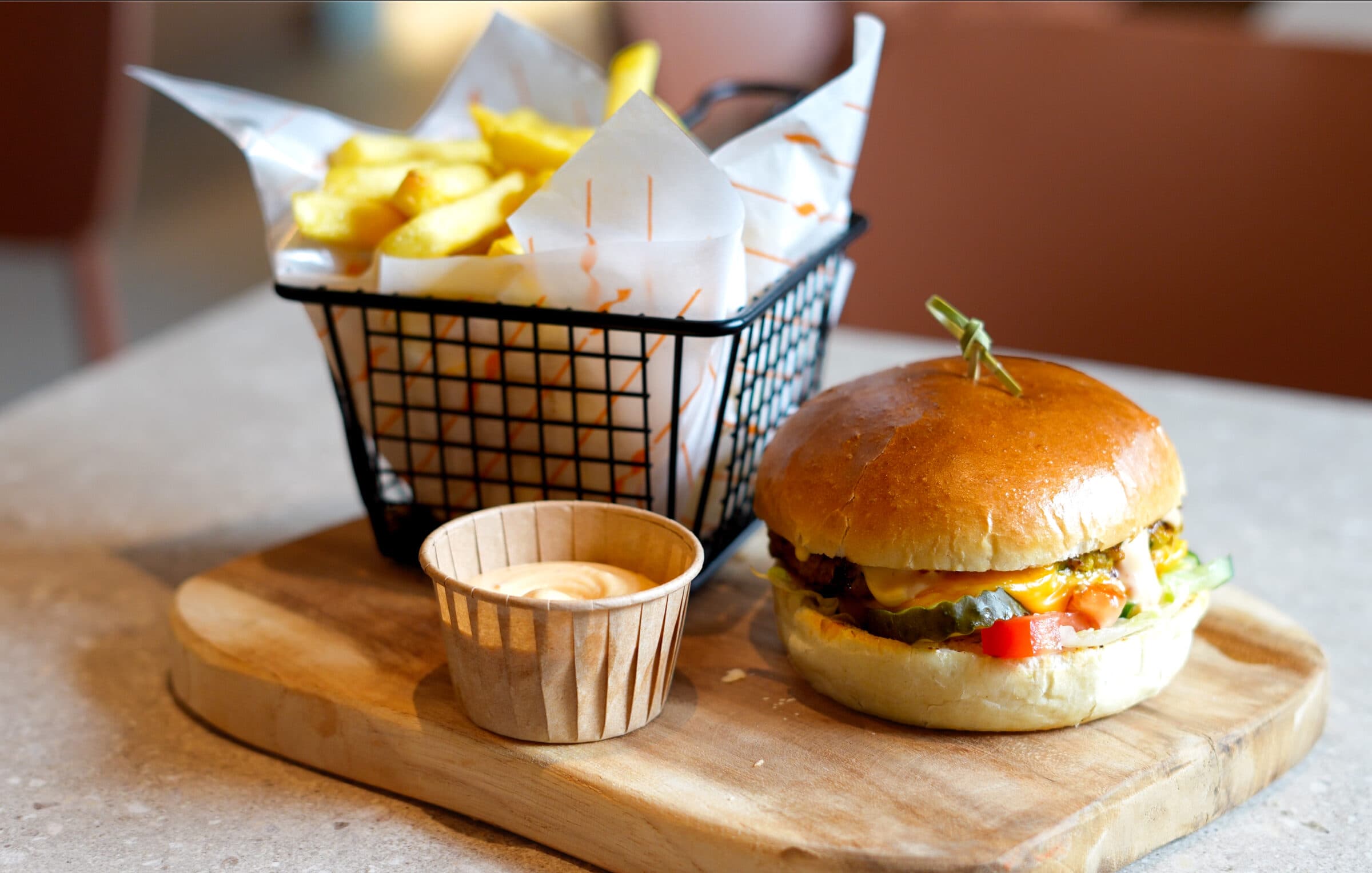 Coja burger op een houten plank, met een mandje dikke friet en een kuipje saus ernaast.
