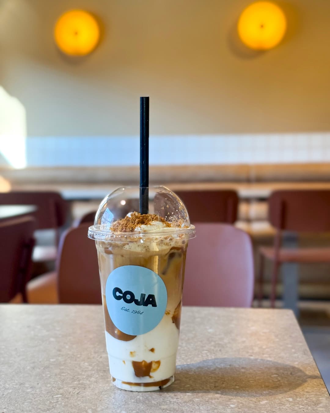 Iced caramel koffie in de warme eetzaal, ronde oranje wandlampen op de achtergrond.