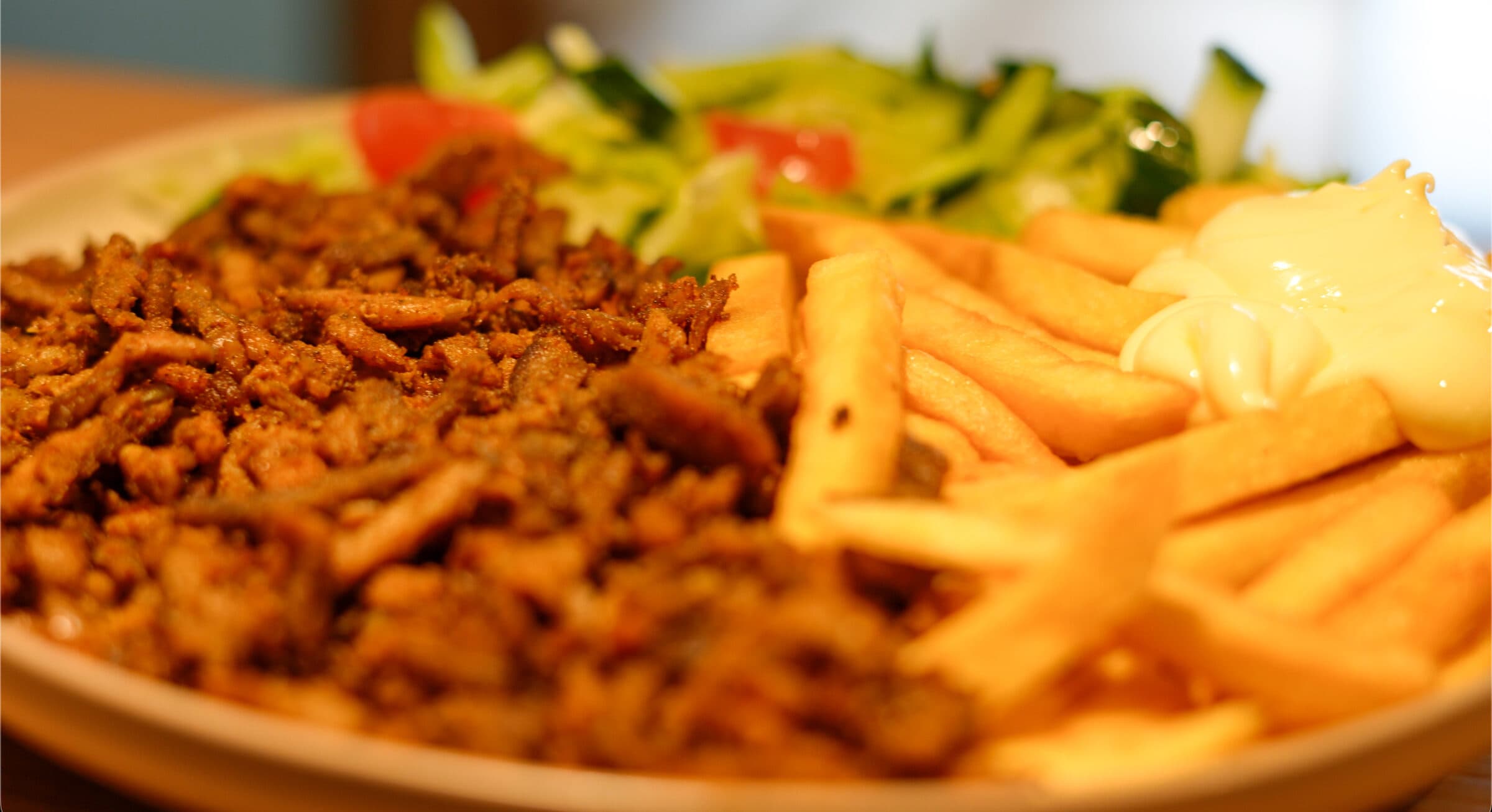 Shoarmavlees met friet, mayonaise en frisse salade op een bord.