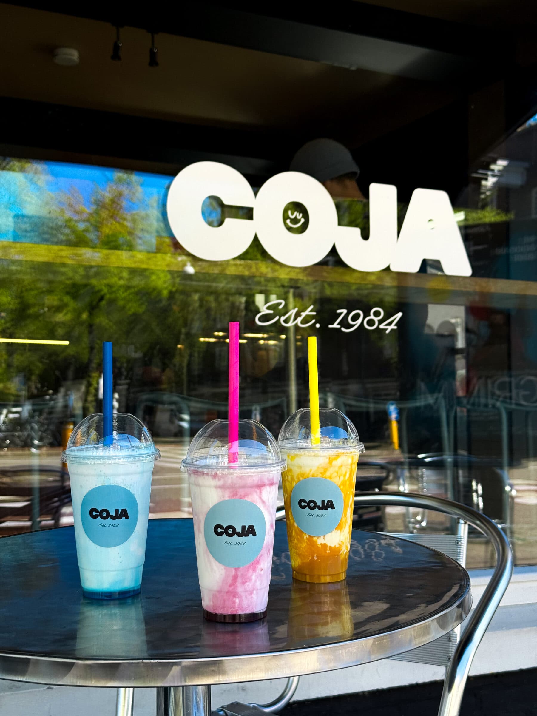 Drie kleurrijke Coja smoothie cups voor het etalageraam, Est. 1984.